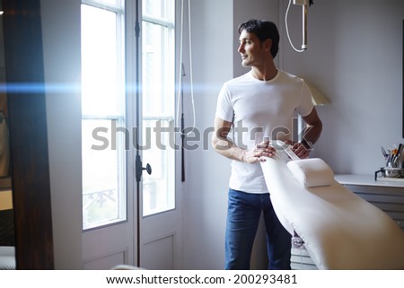 Handsome man in white shirt standing across the window in the cabinet of professional aesthetic clinic, satisfied patient smiling