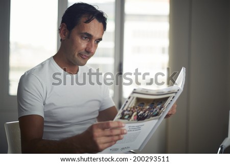 Attractive man in the white t-shirt reading journal sitting in office of private aesthetic clinic