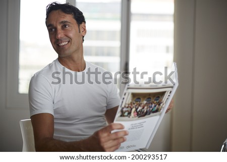 Handsome man in a white shirt sitting in a chair with the journal in hands and smiling, cabinet of aesthetic clinic