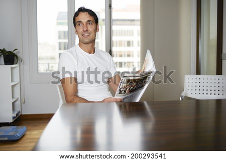 Handsome man with journal in the hands sitting at a table in office of private clinic, window background