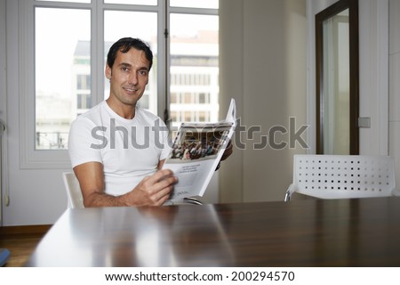 Attractive man sitting in a chair  with the magazine in the hands and smiling
