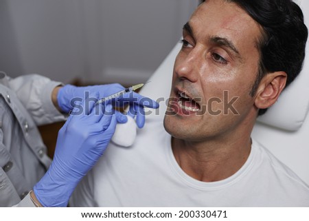 Attractive man being afraid of syringe with needles during cosmetic injection