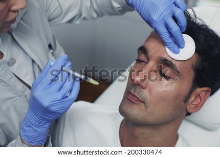 Doctor wipes male face with cotton pad during cosmetic injection with vitamins, rejuvenating