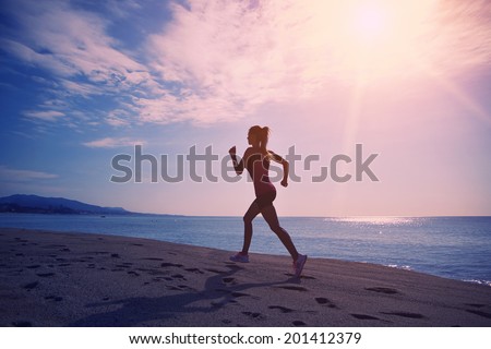 Beautiful female jogger with strong figure run on the sand along the sea ,silhouette of athletic girl on sea and sky background