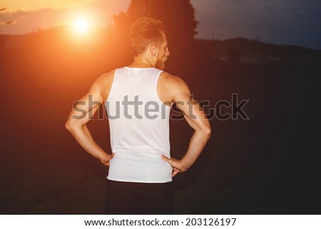 Young male runner in white t-shirt resting after intensive night jogging, beautiful jogger resting in the park at amazing sunset, health lifestyle and fitness concept