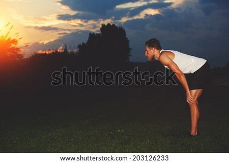 Beautiful muscular jogger enjoying the sunset after evening jogging in the park, health lifestyle and fitness concept