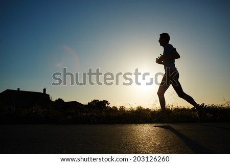 Silhouette of muscular athletic jogger running on the road with at sunset, evening jogging, health lifestyle and fitness concept