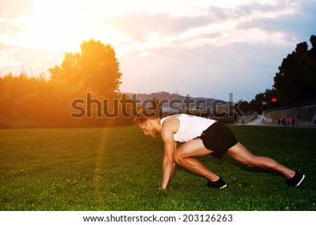 Young male runner with muscular body ready to start standing on the grass, male jogger on the evening jog in the beautiful park, health lifestyle and fitness concept