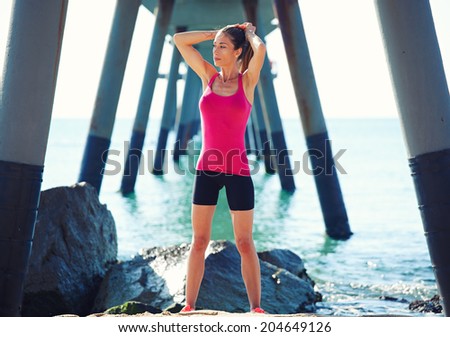 Beautiful female jogger resting after morning run on the beach standing on the beautiful sea background, fitness and healthy lifestyle concept