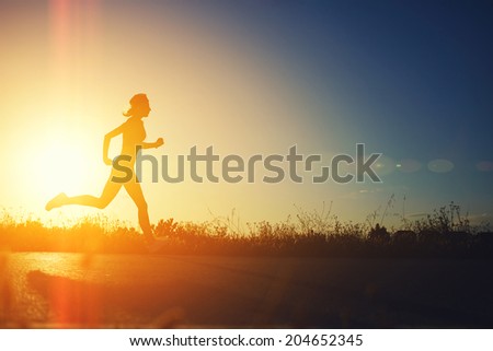 Silhouette of muscular sporty girl running on the beautiful road at amazing bright sunset, female jogger with muscular body at evening run, fitness and healthy lifestyle concept