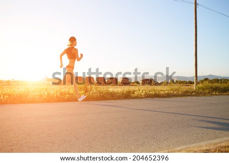 Silhouette of muscular women running on the road at bright orange t sunset, fitness and healthy lifestyle concept