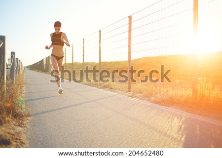 Athletic blond girl with beautiful figure jogging in the park, female runner jogging outdoors at orange sunset, beautiful girl with muscular body doing workout, fitness and healthy lifestyle concept