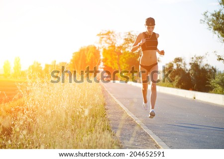 Slim athletic girl at high speed running down the road along beautiful field, evening run outside, beautiful sunset light, fitness and healthy lifestyle concept