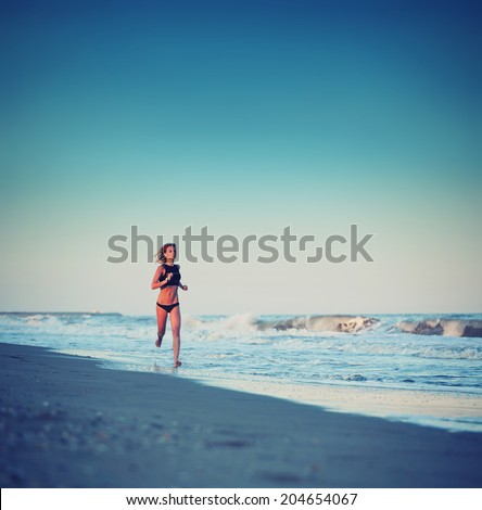 Beautiful female jogger runs along the sea, evening run on the shore, jogging on the beach,  fitness and healthy lifestyle concept