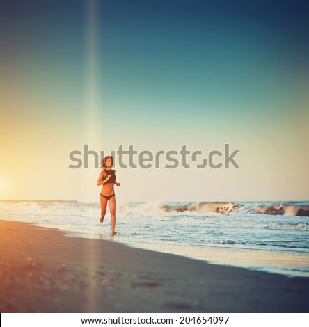 Attractive female runner jogging o the beach touching waves, evening run along the sea, fitness and healthy lifestyle concept