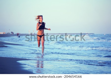 Attractive female runner with muscular body on speed running on the beach, evening run along the sea, fitness and healthy lifestyle concept