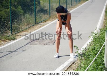 Athletic girl with beautiful figure resting after intensive run, female jogger taking break standing on the park trail, fitness and healthy lifestyle concept