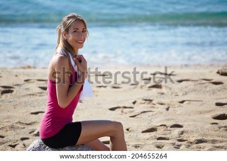 Attractive sports woman with towel in the shoulders resting after morning run on beach, female runner taking break, fitness and healthy lifestyle concept