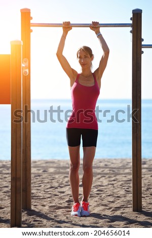 Attractive sporty woman with beautiful figure holding horizontal bar on the beach, stretching exercise on the beach, fitness and healthy lifestyle concept