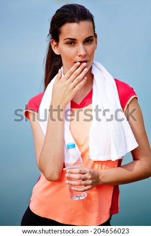 Portrait of beautiful sporty girl with bottle of water and towel, female runner resting after jog, fitness and healthy lifestyle concept