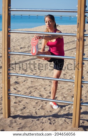 Middle aged woman stretching on the beach before run on the beautiful sea background, fitness and healthy lifestyle concept