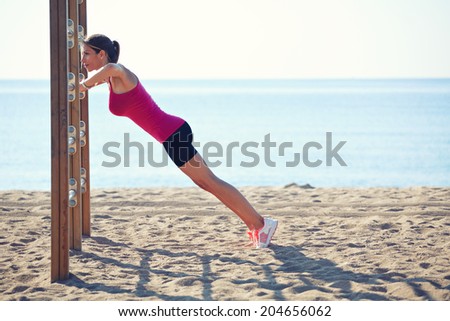Athletic beautiful woman pulls up on the horizontal bar, workout on the beach, female runner   doing exercise on the beach, fitness and healthy lifestyle concept