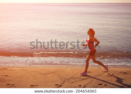 Beautiful female jogger with strong figure run on sand, morning run on the beach, fitness and healthy lifestyle concept