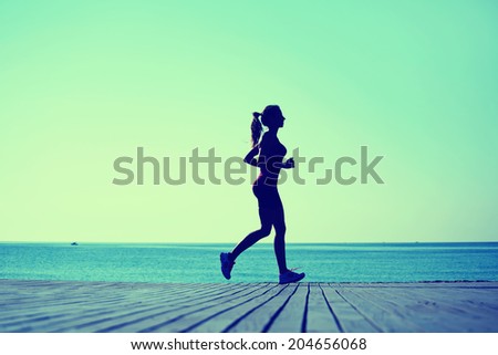 Silhouette of athletic female jogger with beautiful figure running on the pier, morning run on the beach, fitness and healthy lifestyle concept