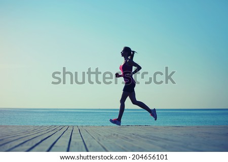 Silhouette of attractive girl with strong body dynamically running at sped on the pier, morning run on the beach, fitness and healthy lifestyle concept