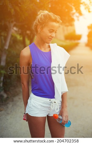 Attractive female runner in bright sportswear resting after evening run in the park, sport outside at amazing sunset, fitness and healthy lifestyle concept
