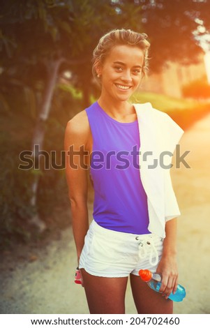 Attractive blond female runner smiling in the beautiful green park ,evening run at sunset , fitness and healthy lifestyle concept