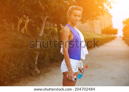 Sporty and athletic blond runner standing at sunset in the park, evening run and sport outside, fitness and healthy lifestyle concept