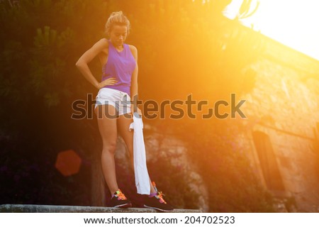 Blond athletic girl resting in the park at beautiful sunset, female runner standing with towel in the hands, evening run in the park, fitness and healthy lifestyle  concept