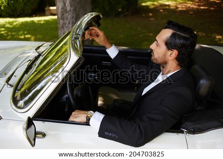 Elegance rich man in black formal wear behind the wheel of cabriolet classic car, lifestyle and successful business concept