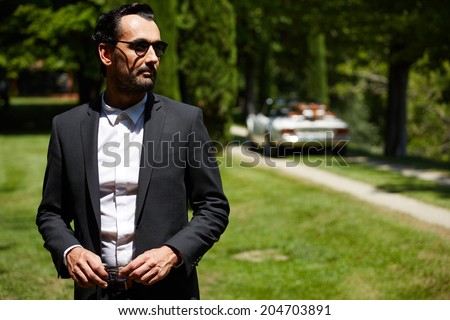 Elegance stylish and successful man at sunny day standing on background of his cabriolet classic car, lifestyle and successful business concept