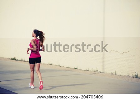 Beautiful sporty girl with muscular athletic body on the morning jogging at sunny day, female jogger runs along pastel color wall, ealthy lifestyle and fitness concept