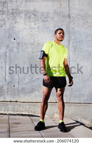 Young muscular build man with running armband on the arm resting tired after run,  attractive athlete resting after workout outdoors, fitness and healthy lifestyle concept