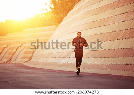 At amazing sunset light muscular build sportsman running along beautiful wall, evening run at beautiful sunset, male runner running at sunset, fitness and healthy lifestyle concept