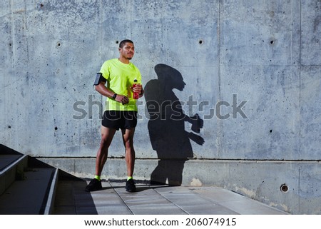 Attractive runner with muscular body resting after intensive run, african-american runner in bright sportswear having a rest after training outdoors, fitness and healthy lifestyle concept
