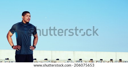 Attractive male runner with muscular body relaxing after training outdoor and enjoying sunset standing on beautiful sky background, portrait of young athlete resting tired after run, fitness concept