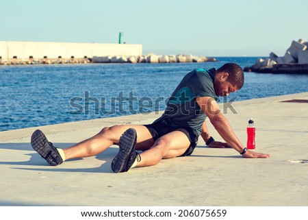 Sportive young male runner doing sit-ups outdoors at evening training, muscular build male runner doing exercise outdoors, workout after run, fitness and healthy lifestyle concept