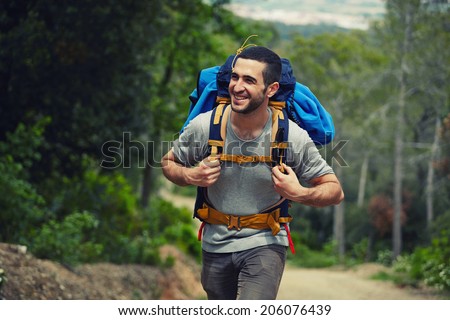 Attractive hiker with big traveling rucksack moving up on the mountain trail and smiling, happy traveler overcome big way smiling looking away, adventure travel and discovery