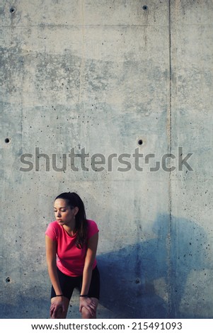 Attractive sporty women taking break after evening run outdoors, fit female athlete resting after running, tired after jogging athletic runner standing on concrete wall background, fitness concept