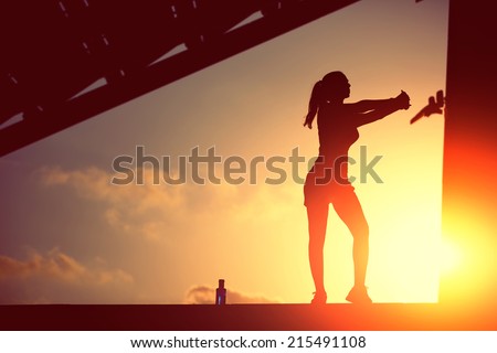 Silhouette of attractive female runner doing stretching exercise on beautiful sunset background, athletic female jogger silhouette against the sunset doing workout, woman fitness silhouette