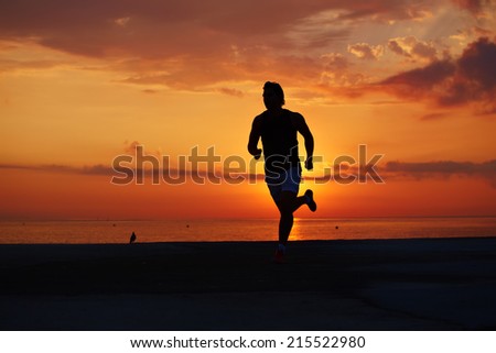 Silhouette of athlete man running early morning on the beach with orange sunrise on background, beautiful runner silhouette in action, fitness and healthy lifestyle concept