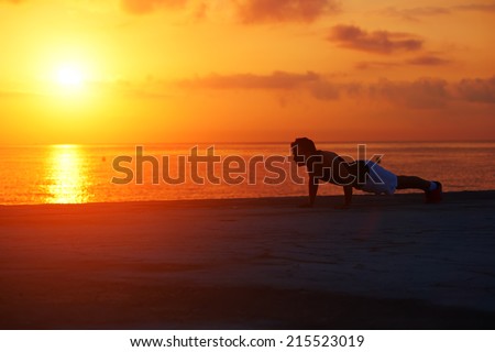 Silhouette of athletic runner warming up and doing some push ups on the beach, push ups or press ups exercise by young male runner man, fitness and healthy lifestyle concept