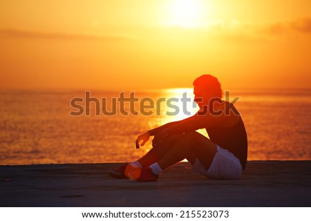 Tired after intensive run athletic runner resting on the beach, male jogger taking break after morning training outdoors, runner resting on colorful sunrise background, healthy lifestyle concept