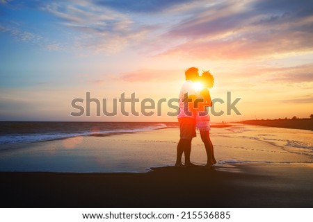 Silhouette of beautiful couple holding hands having romance, valentines day background of couple in love, man and woman kissing on the tropical beach at orange sunset sky, young family at sunset