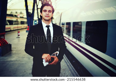 Attractive businessman in big train station, beautiful businessman holding newspaper in the hands, adult man in a suit looking to the camera, businessman waiting for the train in railway station
