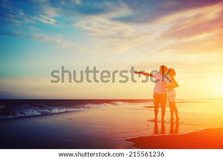 Happy young couple embracing enjoying ocean sunset, man and woman in love standing on the beach with beautiful sunset on background, man and woman in romantic vacation